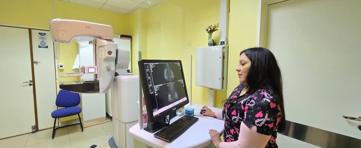Técnica radióloga analizando estudios en una computadora junto a un mamógrafo digital
